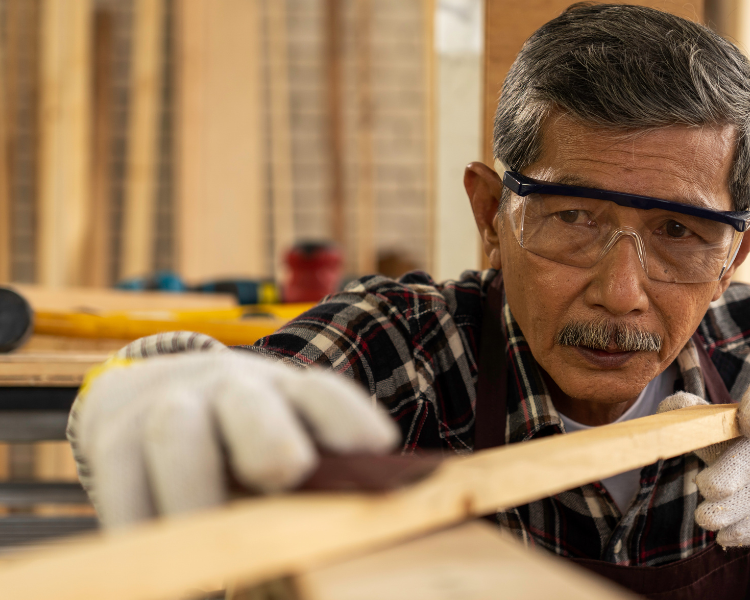 An older, Asian carpenter plaining wood