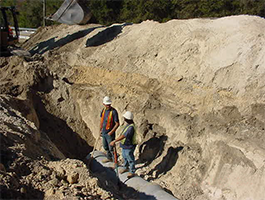 OSHA File photo (March 6, 2002) : Illustrates hazards such as employees working in an unprotected excavation, without a ladder and with debris piled atop the excavation.