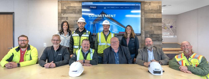 Matthew Thurlby, OSHA Omaha Area Office, with David Cavlovic and Casey Lenners, Sampson Construction and  Jim Cover, NE Onsite Consultation seated at a table with signing ceremony attendees standing behind them.  