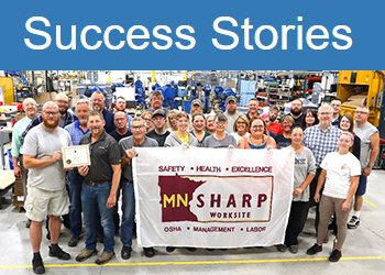Success stories: Gemini Inc. employees stand on their shop floor, proudly holding their SHARP flag