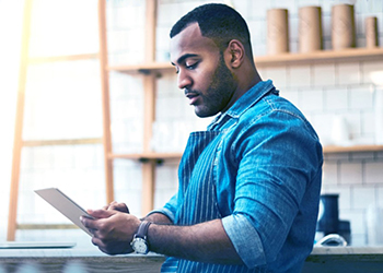 Young male worker in apron, using tablet