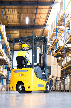 Warehouse worker wearing high-viz vest and hardhat while using a forklift to move pallets