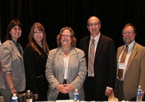 The panel of agency representatives stands for a group photo before the meeting. From left to right: Cdr. Joshua Reynolds (USCG), Staci King (BSEE), Linda Daugherty (PHMSA), Pam Phillips (EPA), David Michaels (OSHA), Glenn Paulson (EPA), and Nathan Frey (OMB).